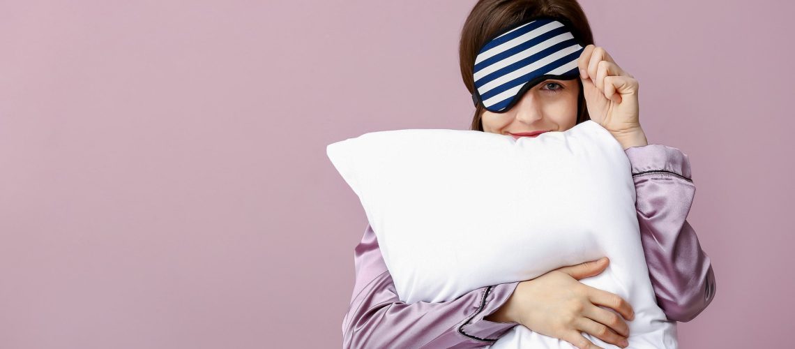 Sleepy woman with mask and pillow on color background