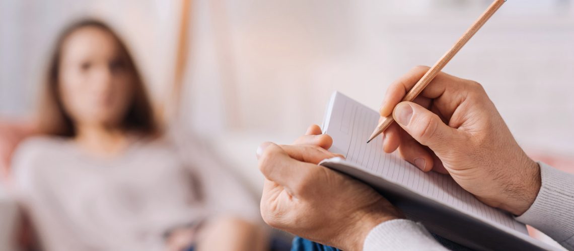Pay attention to details. Selectife focus of pencil in hands of professional psychotherapist holding it and making notes while talkign with his client