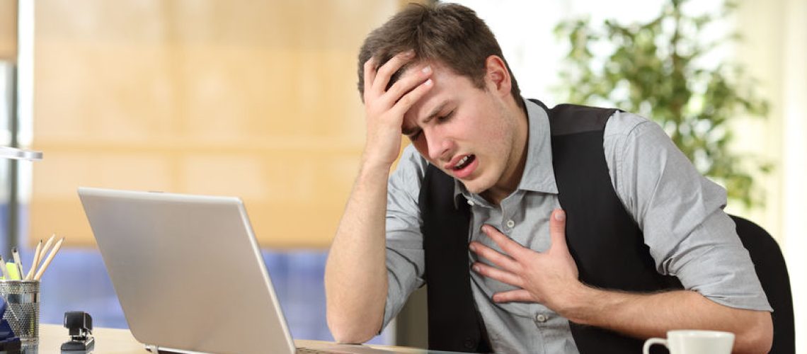 Businessman suffering an anxiety attack with the hands in his chest and head sitting in a desktop at office
