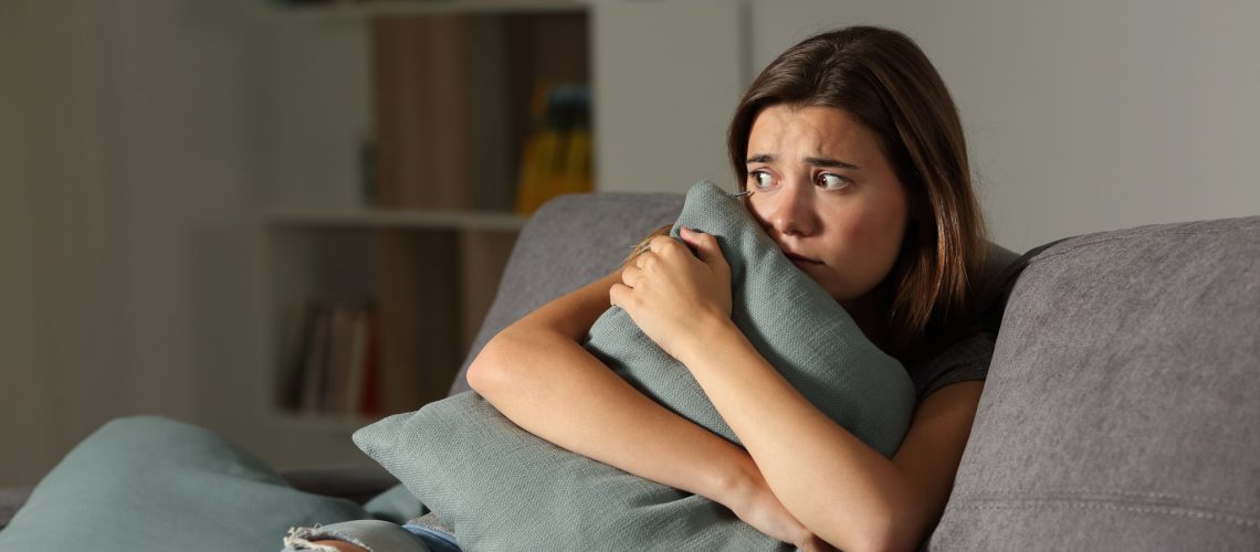Scared teen at home embracing pillow sitting on a couch in the living room at home