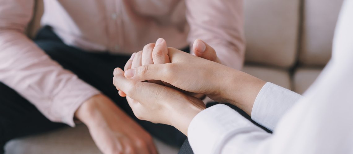 Close-up of psychiatrist hands together holding palm of her patient.  Psychological women comforting and holding a male hand while sitting on the sofa. psychologist concept